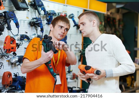 Sale assistant demonstrating electric drill perforator to young man in electrical appliance shopping mall supermarket