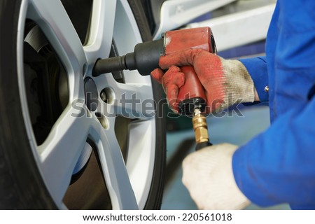 car mechanic screwing or unscrewing car wheel of lifted automobile at repair service station