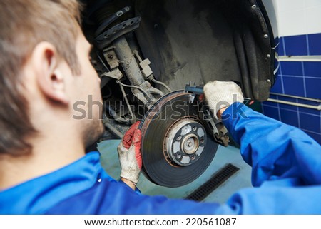 car mechanic examining car wheel brake disc and shoes of lifted automobile at repair service station