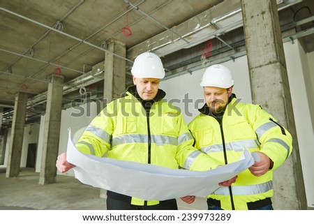 young male engeneers workers foreman at a indoors building site with blueprints