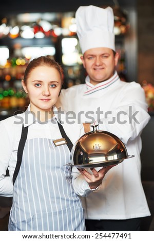 Waitress with tray cloche and cook chef at the indoor restaurant service