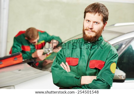 Automobile glazier repairman portrait in front of worker repairing car windscreen in auto service station garage