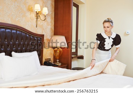 Hotel service. female housekeeping worker maid making bed with bedclothes at inn room