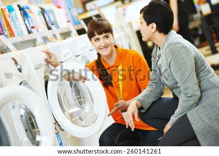 Young female seller assistant helps woman to choose washing machine in home appliance shopping mall supermarket