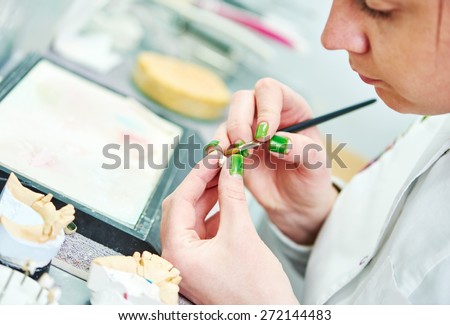 Dental technician painting tooth during work on dentures at prosthesis laboratory