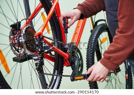 Bike service: mechanic serviceman repairman tuning and assembling or adjusting bicycle chain in workshop