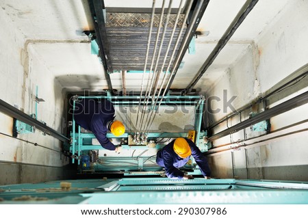 two male technician machinist worker at work adjusting elevator mechanism of lift with spanner
