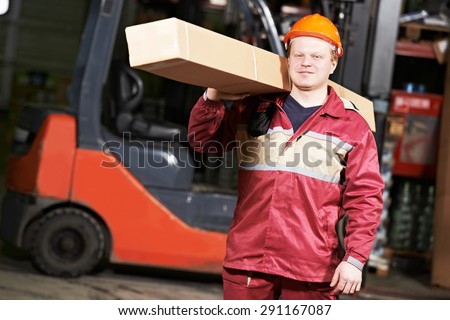 young warehouse worker in uniform in front of forklift stacker loader with box