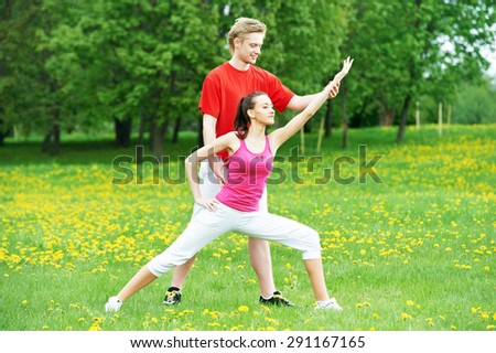 Young fitness woman and male instructor doing physical stretching exercises during outdoors sport training