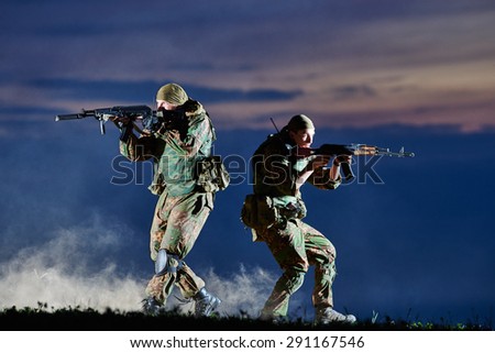 military. two soldiers in uniform running with assault rifle weapon on sunset during attack outdoors. Authentic shooting in challenging conditions. Maybe little blurred.