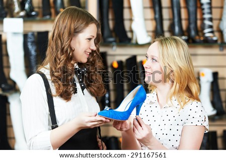 Young woman and seller assistant choosing footwear during shopping at shoe shop