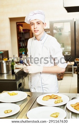 young male cook chef with food on the plate in commercial kitchen