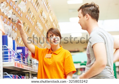 Young female assistant seller helps purchaser choosing lamp in hardware shopping mall supermarket