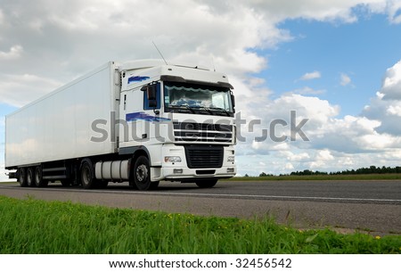 white lorry with white trailer on the highway over blue cloudy sky
