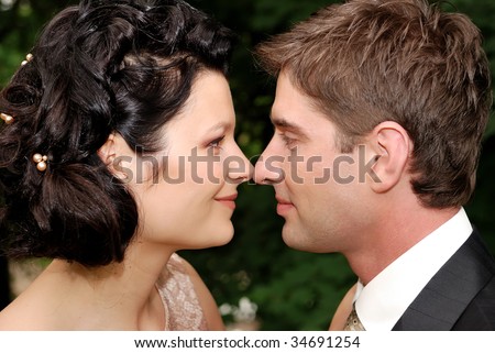 Close-up photo of young wedding couple. They are looking at each other and slightly touching with noses.