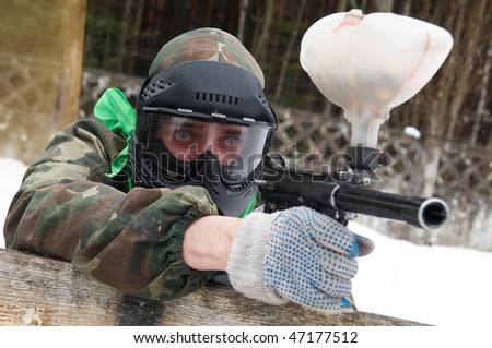 paintball sport player with mask aiming gun and shooting to enemy in winter