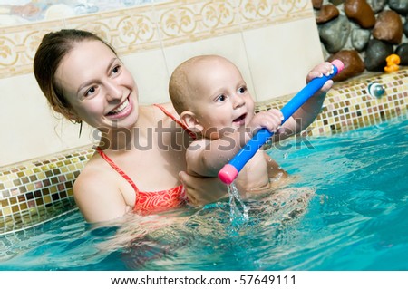 Mother and baby child playing in a swimming pool. DOF focus on babys face with mother slightly defocused in the background.