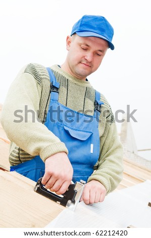 builder worker at roofing works on tiling with staple gun