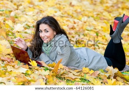 One young pretty student girl in yellow autumn leaves with computer laptop