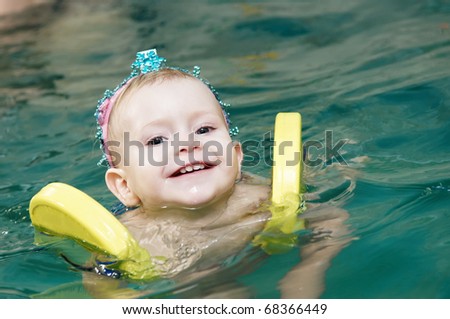 One happy smiling little girl swimming with safety discs at water pool
