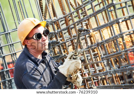 worker in protective glasses cutting concrete reinforcing metal rods at construction building site