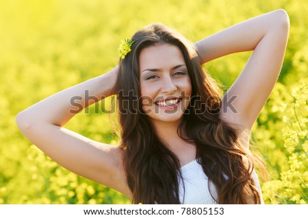 Happy smiling young woman with hands behind head over yellow green rapeseed meadow