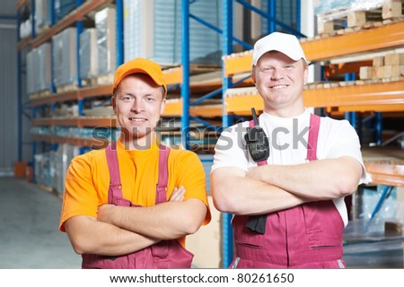 two young handsome workers man in uniform in front of warehouse rack arrangement stillages