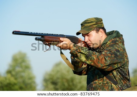 Male hunter in camouflage clothes on the field aiming the hunting rifle during a hunt.