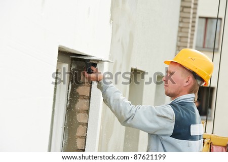 Plasterer facade builder worker with scratching tool at thermal insulation works