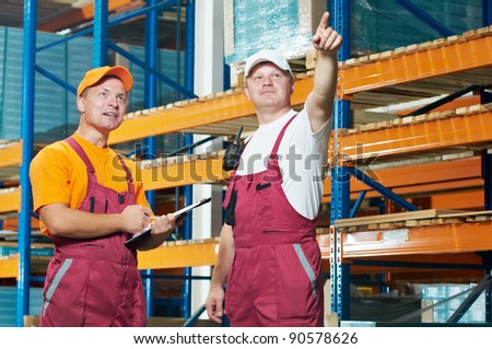 two young workers man in uniform in front of warehouse rack arrangement stillages