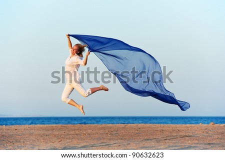 Happy woman jumping on sea beach with blue flying silk cloth