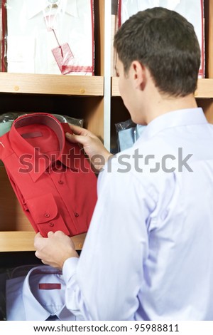 Young man choosing shirt for suit during apparel shopping at clothing store