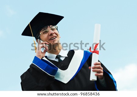 Happy graduate student in gown with diploma speaking on phone over blue sky