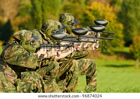paintball extreme sport players team in protective camouflage uniform and mask with markers gun in summer field