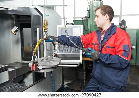 manufacture worker moving detail by beam crane into modern cnc machine tool for metal cutting processing at factory workshop