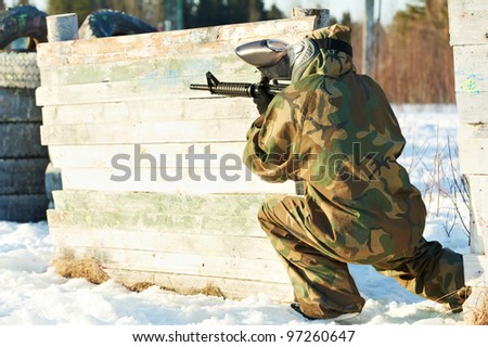 paintball extreme sport player wearing protective mask and comouflage clothing with marker gun at winter outdoors