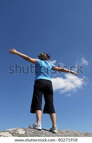 young woman with arms wide open against blue sky