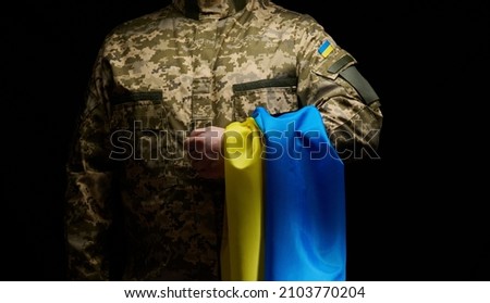 a soldier of the Ukrainian armed forces stands with a blue-yellow flag of Ukraine on a black background. Honoring veterans and commemorating those killed in the war Stockfoto © 