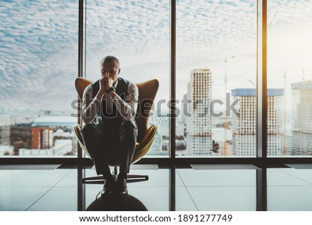 A portrait of a man entrepreneur in a state of worry and dismay sitting on an armchair in front of the window of a luxury office high-rise and thinking about how to solve recent business issues Foto d'archivio © 