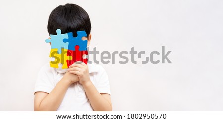 Autism awareness day April 2 - Studio Portrait of a little cute asian child cover his face with the colorful puzzles pieces. Autism Spectrum Disorder concept, ASD, Syndrome, Symptoms, Copy space