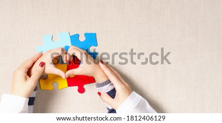 World autism awareness day, understanding  love concept, a beautiful mother holding hands of little autistic child making heart shape over symbol colored puzzle. ASD, April 2, Top view banner.