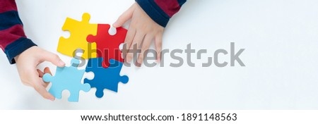 Top view hands of a little child arranging color puzzle symbol of public awareness for autism spectrum disorder. World Autism Awareness Day, ASD, Caring, Speak out, Campaign, Togetherness. Banner.