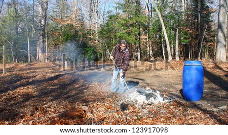 A man working a burning pile of trash and debris along side the edge of the woods