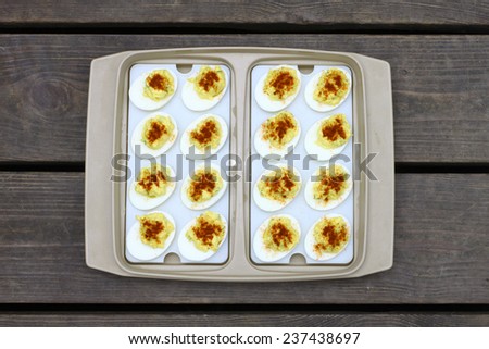 Fresh made deviled eggs in a plastic container made just for deviled eggs on an old wooden weathered picnic tabletop