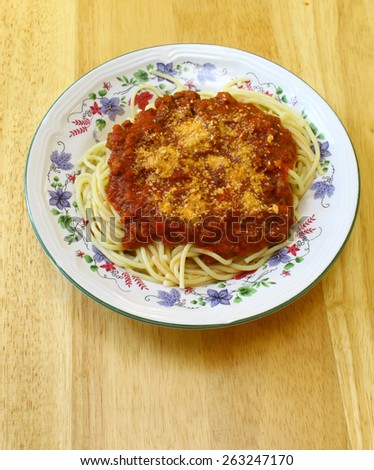 Spaghetti being served on a ceramic dish on a light colored wooden table top