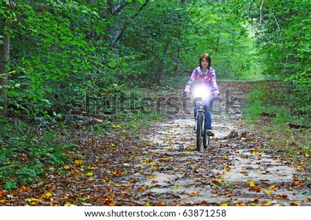A young girl riding a mountain bike through the woods on a trail with a headlight turned on with room for your text