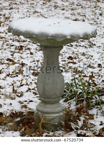 A snow filled birdbath outside on a winter day in the yard covered with a light snowfall with room for your text.