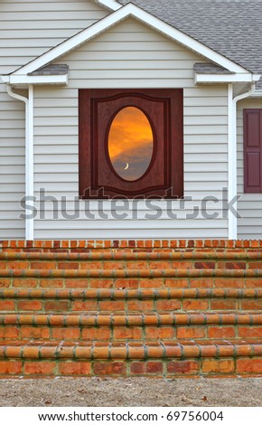 A beautiful sunset with the moon in it reflecting in a window in a vinyl sided house with a brick staircase leading up to it on the back porch along with gutters on both sides with room for your text.