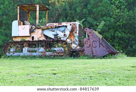 A high contrast picture of an antique vintage old and rusted weed and plant overgrown Bulldozer in a field outside.