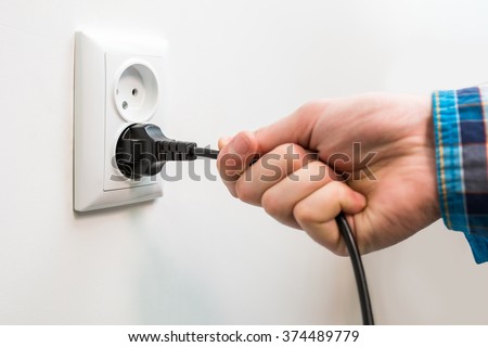 A male hand is pulling an electrical cord plugged into a socket 商業照片 © 